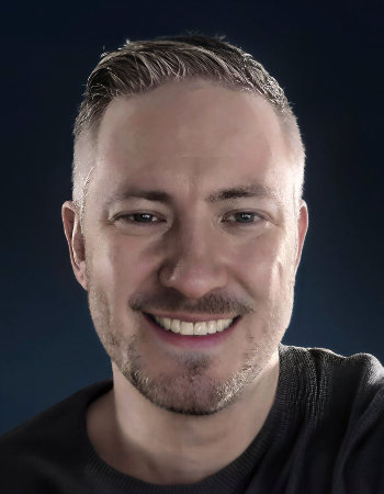 Portrait of Evan Smith. Muted colors, dark background, and smiling face